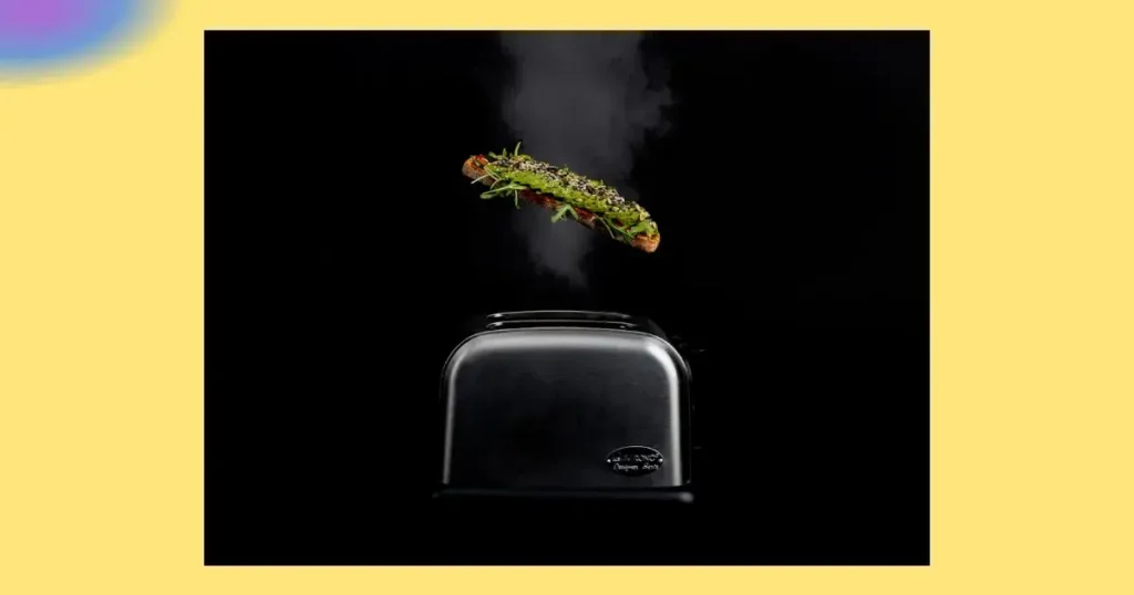 Aus einem metallischen Toaster springt eine Scheibe geröstetes Brot mit Kräutern heraus, aus der Dampf aufsteigt, vor einem schwarzen Hintergrund, der von einem gelben Rand umrandet ist.